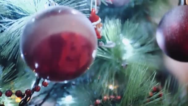 人工的なクリスマスツリーにかかっているいくつかの赤いプラスチック製のクリスマスのおもちゃを閉じます。ストックビデオだ。カラフルな装飾やガーランド。色のクリスマスの装飾。バブルだ。明けましておめでとうございます — ストック動画