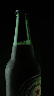 İtalya, Roma - 23. 06 numara. 2021 dikey video. Yeşil Heineken birasının kapağı siyah arka planda dönüyor. Görüntüleri ayır. Alman birası ayna masasında kendi etrafında döner..