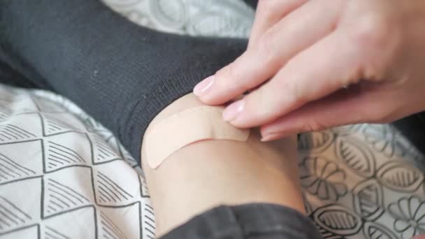 Close up of female hands attaching sticky bandage to leg after wearing new shoes. The girl provides first aid. The girl injured her leg. — Stockvideo