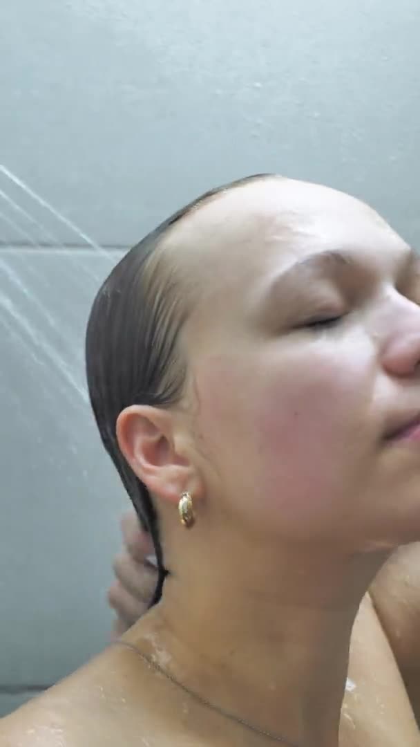Pandangan belakang menutup seorang wanita muda kaukasia dengan rambut panjang berdiri di bawah shower di kamar mandi, mencuci dan mencuci rambutnya, gerakan lambat — Stok Video