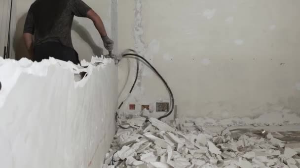 Ο εργάτης καταστρέφει τον εσωτερικό τοίχο με μια βαριοπούλα. Η έννοια της διάλυσης και της ανασυγκρότησης. Ο τοίχος από γυψοσανίδες καταρρέει. Βίντεο 4k — Αρχείο Βίντεο