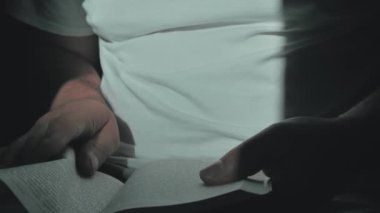 Adam, beyaz masa uçlarında oturan sarı narin sayfaları olan büyük bir kitabın üzerinde okuyor ve parmaklarını çalıştırıyor. Kapat.