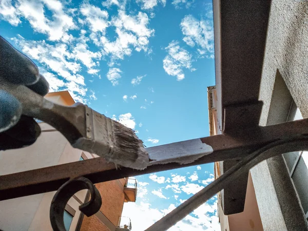 Pracovník se štětcem kreslí kovový plot na pozadí oblohy — Stock fotografie