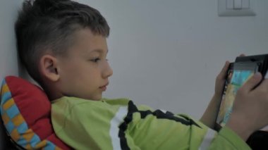 Çocuk halıya uzanıyor ve dijital tablet kullanıyor. Çocuk elinde bir tablet tutuyor.