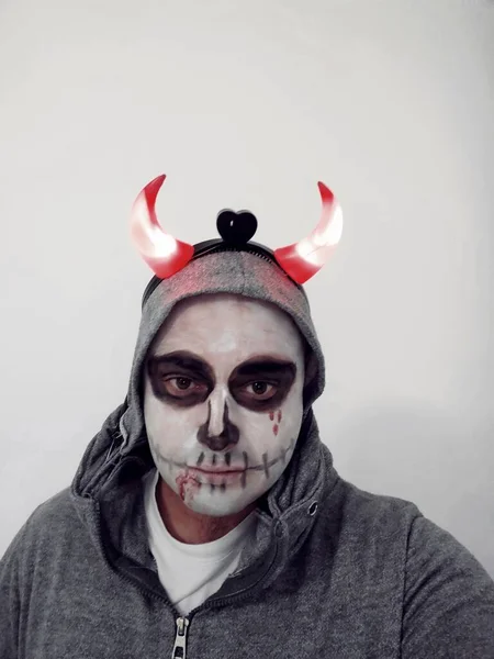 A young man with a painted skull on his face on a white background. Celebration of the Day of the Dead.
