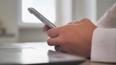 at workplace using smartphone, texting, choose and buy goods and services online, concept of using modern technology. Close-up of female hands holding mobile phone sitting at table.