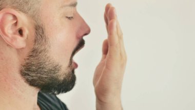 Bad breath. The concept of halitosis. A young man checks his breath with his hand.