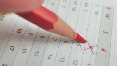 The month number calendar is cut out. Male hand write the day on a paper calendar with a red pen. A very important date in the calendar. Signing the day in the calendar