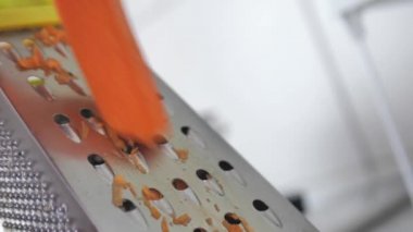 female hands rub carrots on the table. rubbing carrots with a grater at home in the kitchen. close Cutting board. Chop the root of the vegetable into pieces