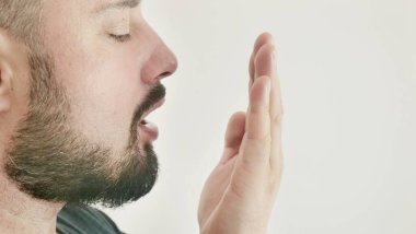 Bad breath. The concept of halitosis. A young man checks his breath with his hand.