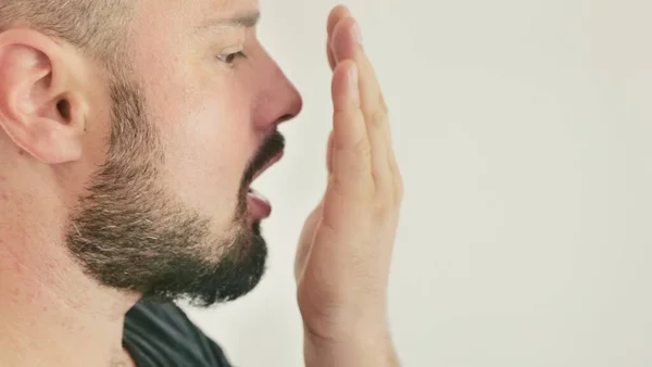 Nefesi kokuyor. Ağız kokusu kavramı. Genç bir adam eliyle nefesini kontrol eder..
