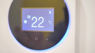 A mans hand presses the buttons on the control of the split air conditioner to turn it on at the recommended temperature.