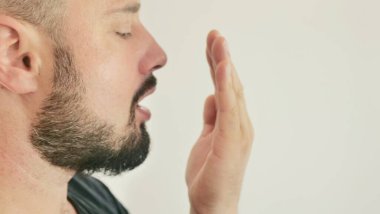 Bad breath. The concept of halitosis. A young man checks his breath with his hand.