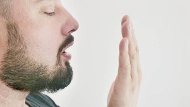 Bad breath. The concept of halitosis. A young man checks his breath with his hand.