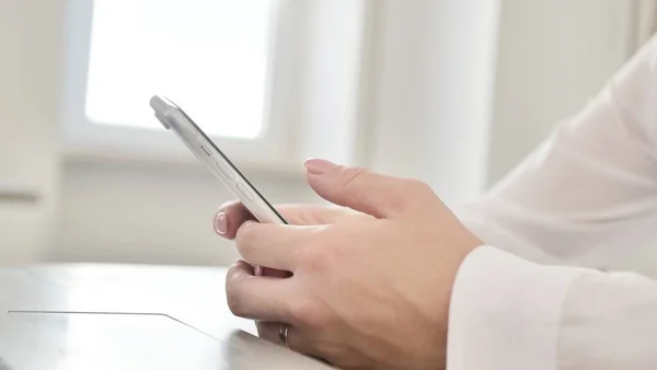 Close-up shot of female hands with smartphone and laptop.