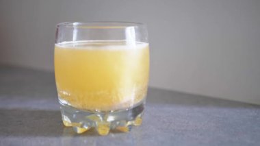 C vitamini beyaz zemin üzerinde bir bardak suya düşer.
