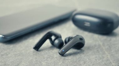 Koyu arka plan üzerinde mavi cep telefonu ile siyah kablosuz kulaklıklar. Case şarj ile modern radyo earphones düz yatıyordu görünümünü. Case şarj yakınındaki Tws kulaklık.