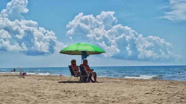 an elderly couple under an umbrella on the beach.