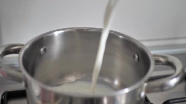 Ev Mutfağı 'nda ocağın üzerine süt dökülüyor. Genç kadın yulaf ezmesi pişirmek için bir tavaya süt döküyor. Sağlıklı yiyecekler, yemek, diyet konsepti.