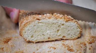 Ekmeği susam tohumuyla kesmeye yakın çekim. Bir adamın eli ekmek bıçağını kesmek ya da dilimlemek için hamburger ekmeği tutar..