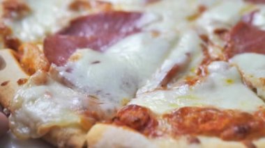 Spatula ile salamlı pizza dilimi almak. Sıcak erimiş peynir esniyor, yakın plan. Fast food konsepti.