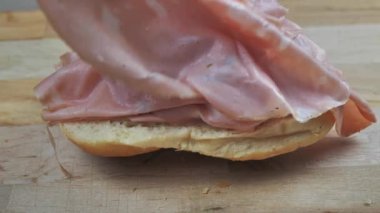 Sandviç hazırlayan bir adamın eli, ekmeğin üzerine mortadella sosisi koyar..