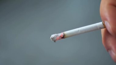 Beyaz arka planda yanan bir sigarayı tutan bir adam..