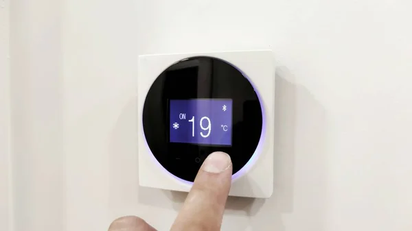 Duvara monte edilmiş dijital klima kontrolü, modern ve modern ev kavramını kontrol eden ev termostatı. Parmaklar rahat bir sıcaklık ayarlar, oturma odasındaki dereceleri ayarlar.