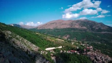 Güneşli Abruzzo 'da dağların ve yeşilliklerin ortasındaki çıplak bir vadi etrafındaki hava manzarası. İtalya İHA atışının etrafında dönüyor