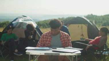 Meşgul yakışıklı Afro-Amerikan gezginler kampta tablet bilgisayar ve belgelerle çalışıyorlar.