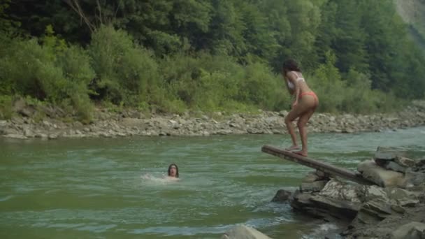 Беззаботные многокультурные люди, ныряющие в горную реку с трамплина — стоковое видео