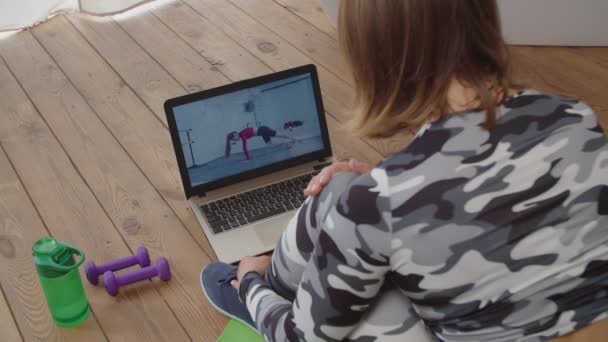 Achteraanzicht van vrij sportieve vrouwelijke kijken tutorial fitness video online op laptop thuis — Stockvideo