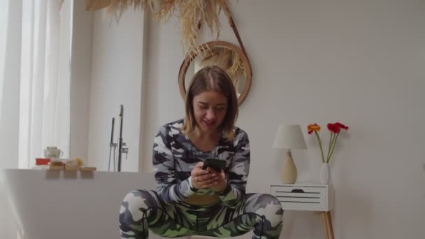 Ziemlich aktive, sportlich fitte Frauen hocken und vernetzen zu Hause auf dem Smartphone — Stockvideo
