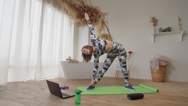 Behoorlijk sportieve fitness vrouw aan het trainen uit draaiing driehoek pose tijdens online yoga les — Stockvideo