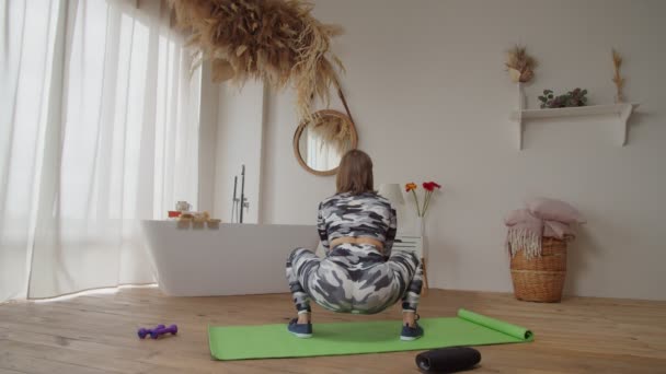 Achteraanzicht van actieve sportieve fitte vrouw die hurktraining uitvoert in huiselijke ruimte — Stockvideo
