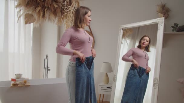 Orgogliosa donna sottile positiva mostrando vecchi jeans oversize dopo la perdita di peso in casa — Video Stock