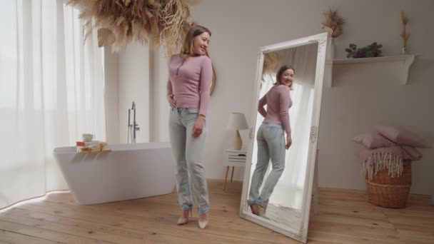Уверенная в себе счастливая красивая женщина проверяет свой внешний вид и идеальную форму тела в зеркале дома — стоковое видео