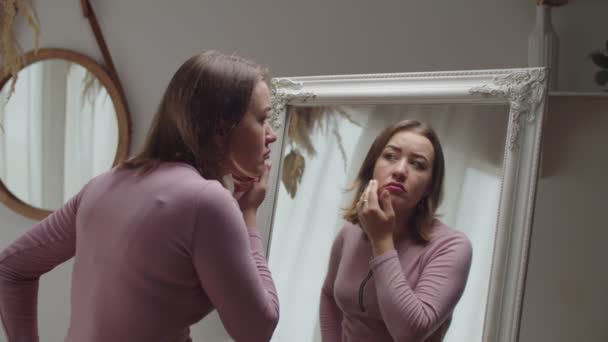 Unzufriedene bezaubernde erwachsene Frau blickt besorgt in den Spiegel über Falten und Hautalterung — Stockvideo