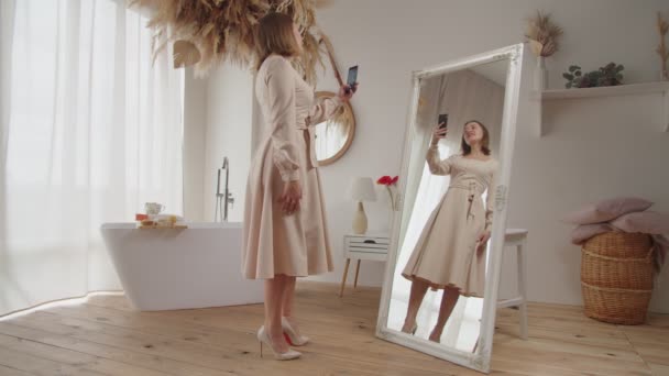 Alegre mujer guapa en vestido nuevo tomando selfie en el teléfono celular delante del espejo — Vídeo de stock