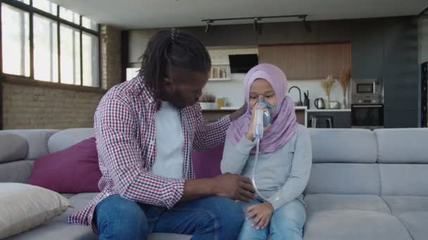 Linda niña afroamericana preadolescente enferma en hijab haciendo inhalación con nebulizador en casa — Vídeo de stock