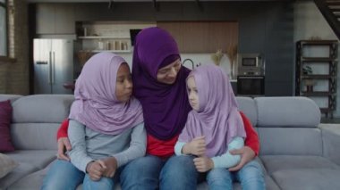 Sevgi dolu Arap kadın tesettürde iki tatlı melez kızı kucaklıyor.