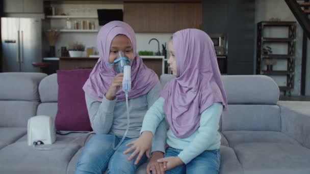 Fürsorgliche jüngere arabische Schwester tröstet krankes Mädchen während Inhalationsmedikation mit Vernebler — Stockvideo