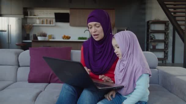 Alegre árabe hijab mamá y adorable niña la creación de redes en línea en el ordenador portátil PC en el interior. — Vídeos de Stock