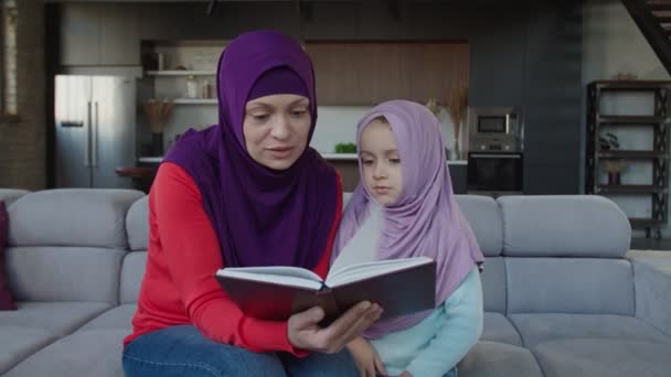 Amor encantadora madre musulmana y linda niña leyendo libro juntos en casa — Vídeo de stock