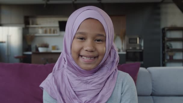 Alegre sorrindo afro-americano muçulmano elementar idade menina no hijab posando em casa — Vídeo de Stock