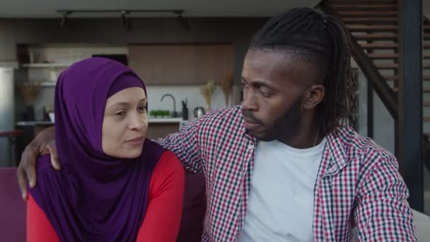 Aantrekkelijke multi-etnische moslim paar praten en hechting op de bank in de huiselijke ruimte — Stockvideo