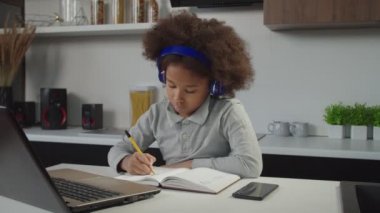 Sevimli okul çağında kulaklıklı Afro-Amerikan bir kız. Evde bilgisayar kullanarak öğreniyor.