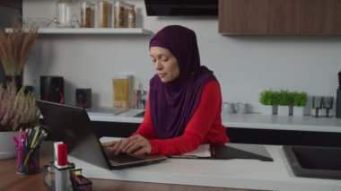 Güzel Müslüman kadın girişimcinin portresi dizüstü bilgisayarda yazarken evde başlangıç çalışması yapıyor.