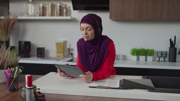 Exitosa mujer de negocios árabe bonita en hijab con auriculares haciendo videollamada en la tableta PC en interiores — Vídeos de Stock