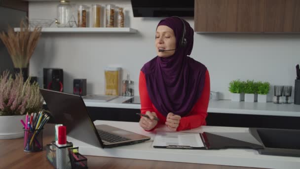 Vänlig härlig muslim kvinnlig kundsupport telefonoperatör med headset arbetar hemma — Stockvideo